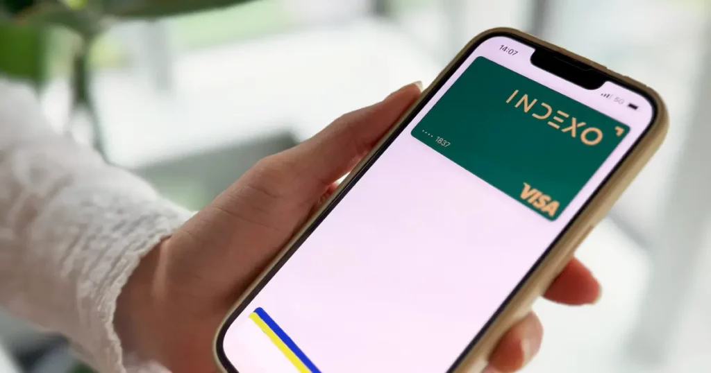 Roka, kas tur viedtālruni, kura ekrānā redzama zaļa digitālā INDEXO karte.