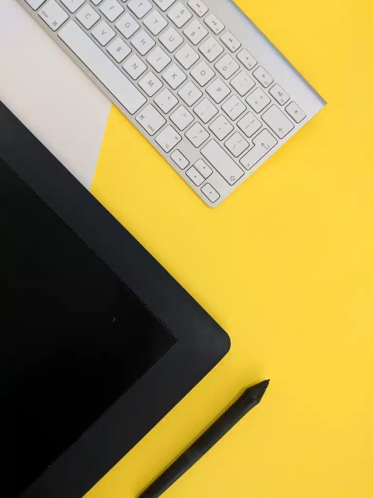 White keyboard, black graphics tablet, and stylus on a yellow and white background.