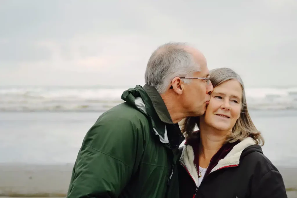 An older man kissing an older woman on a cloudy beach