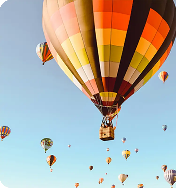Several colorful hot air balloons floating in a clear blue sky, with one prominent balloon in the foreground.