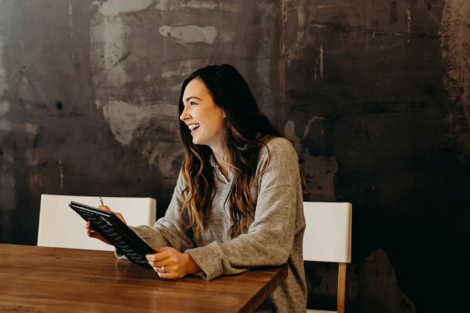 A woman smiling while working on a table and sitting inside