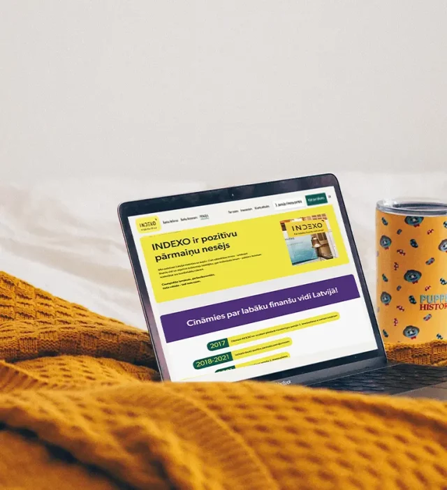 A laptop displaying a financial website, next to a mug, on a yellow knitted blanket.