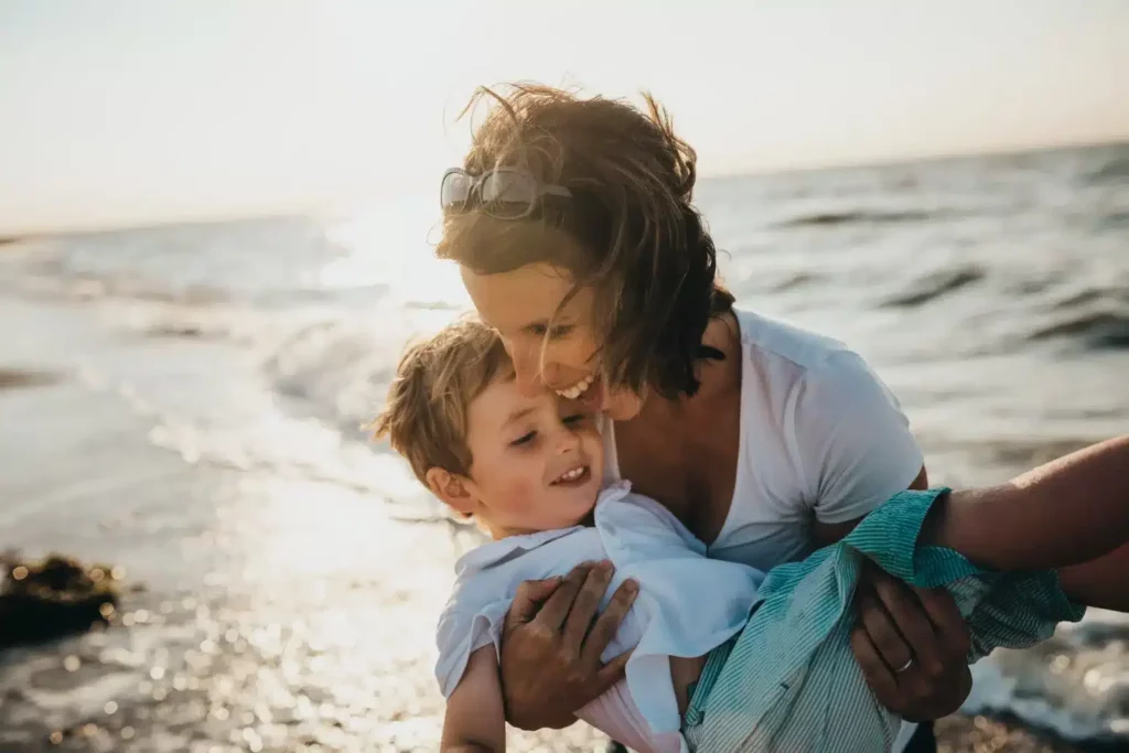 A woman holding a young boy on a sunny beach wearing white